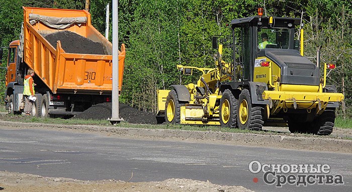 Грейдер НВМ с установленной системой лазерного нивелирования разравнивает асфальтобетонную смесь перед ее уплотнением